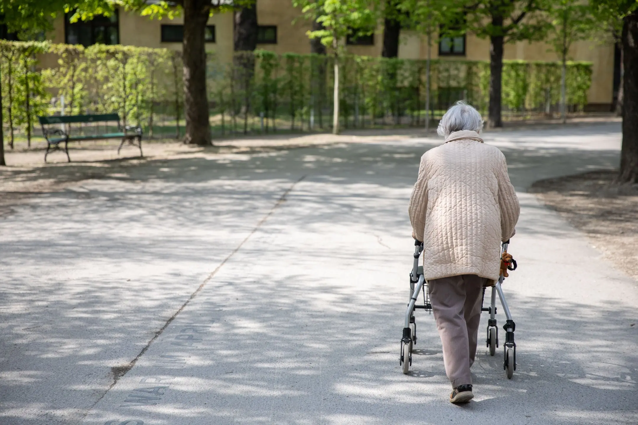 Eine Pensionistin geht im Park mit einem Rollator spazieren.