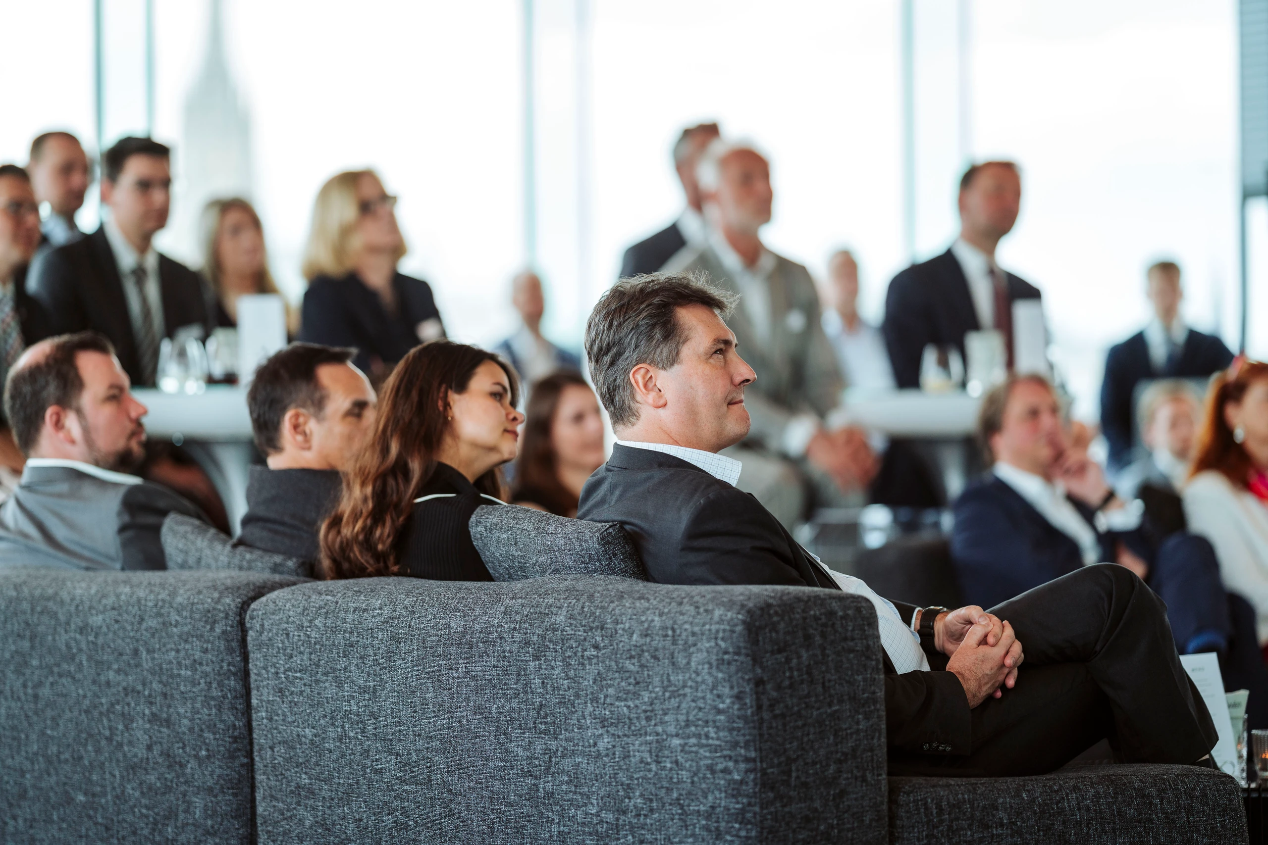 Bild von Nadine Studeny: Geschäftsleute sitzen auf einer Konferenz und hören aufmerksam zu. Fokus auf einen Mann im Vordergrund.