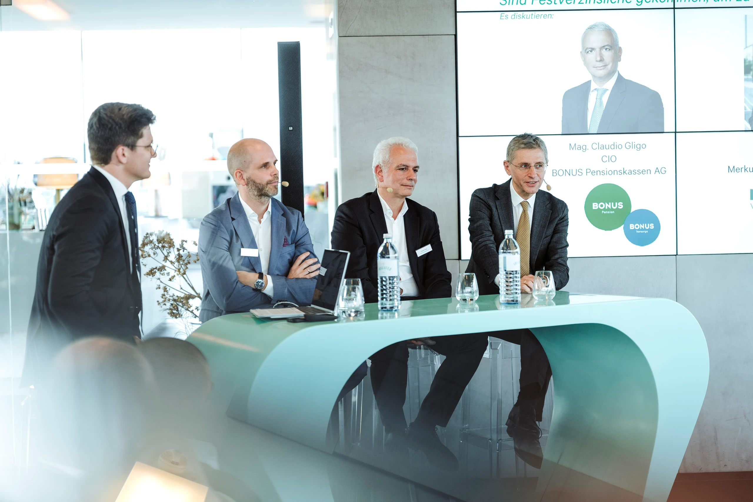 Foto einer Podiumsdiskussion mit vier Geschäftsleuten an einem hellblauen Tisch. Hintergrund: Präsentation mit BONUS Pensionskassen AG Logo. © Nadine Studeny