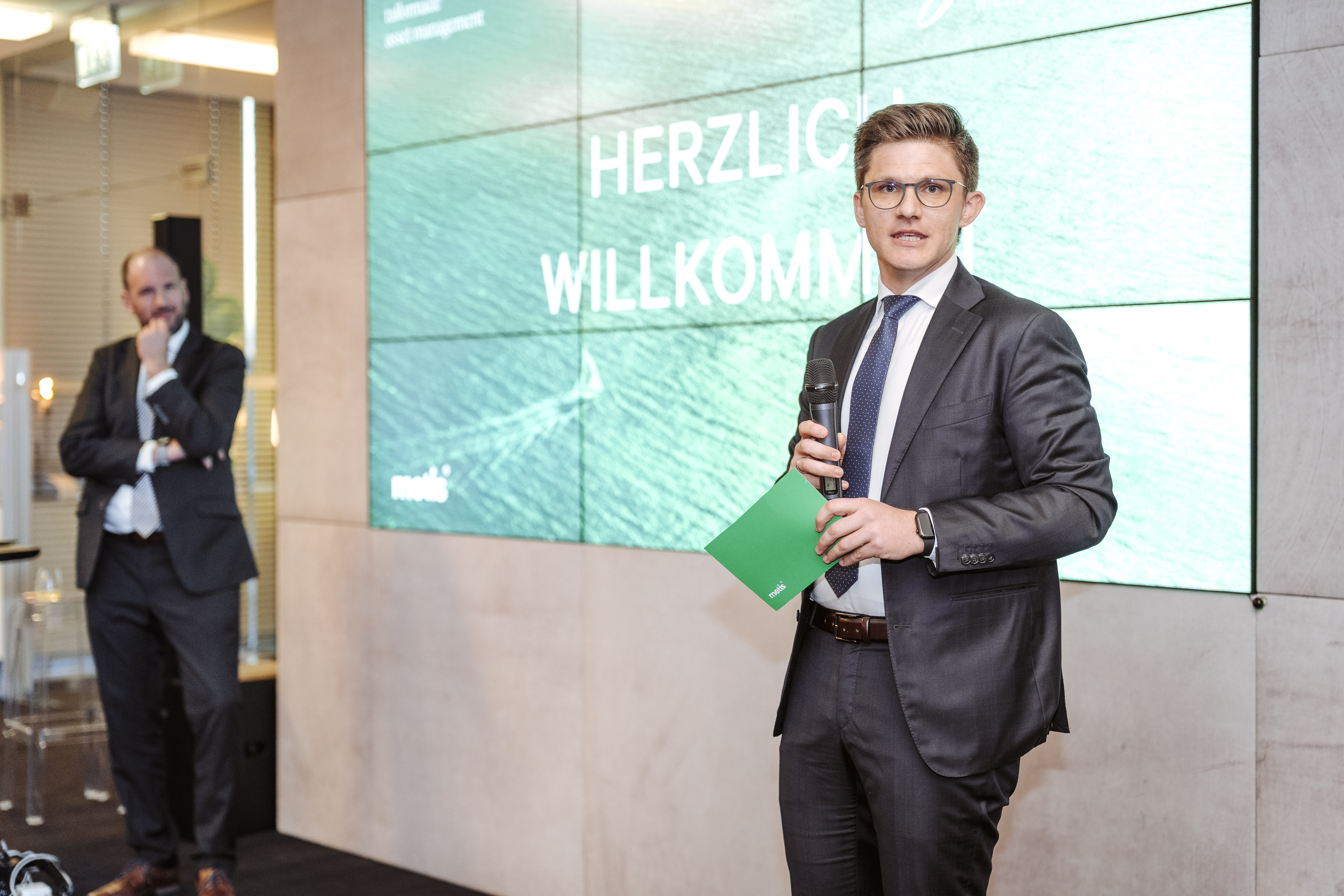 Mann im Anzug hält Präsentation, Herzlich Willkommen auf Bildschirm, © Nadine Studeny