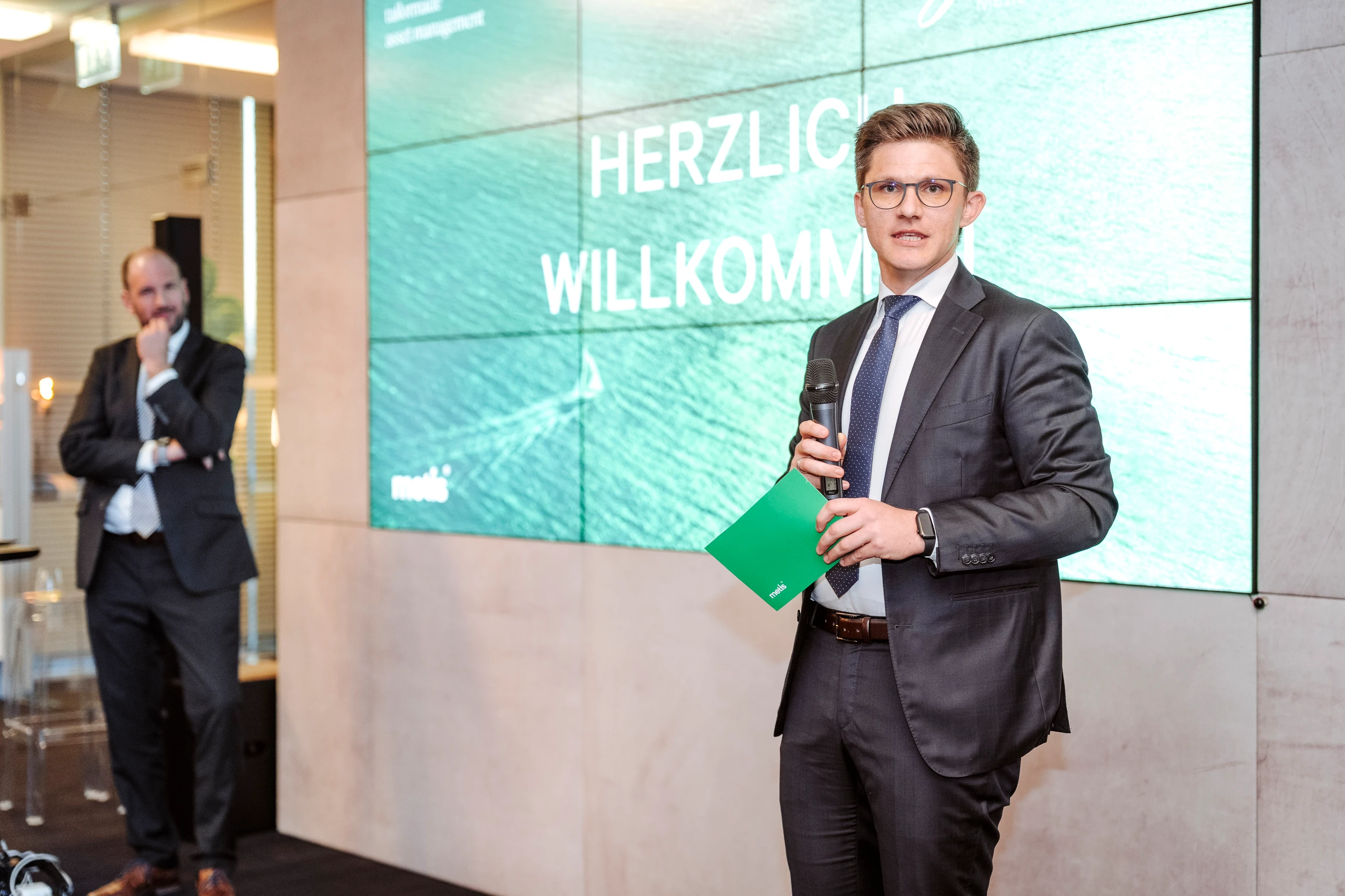 Mann im Anzug hält Präsentation, Herzlich Willkommen auf Bildschirm, © Nadine Studeny