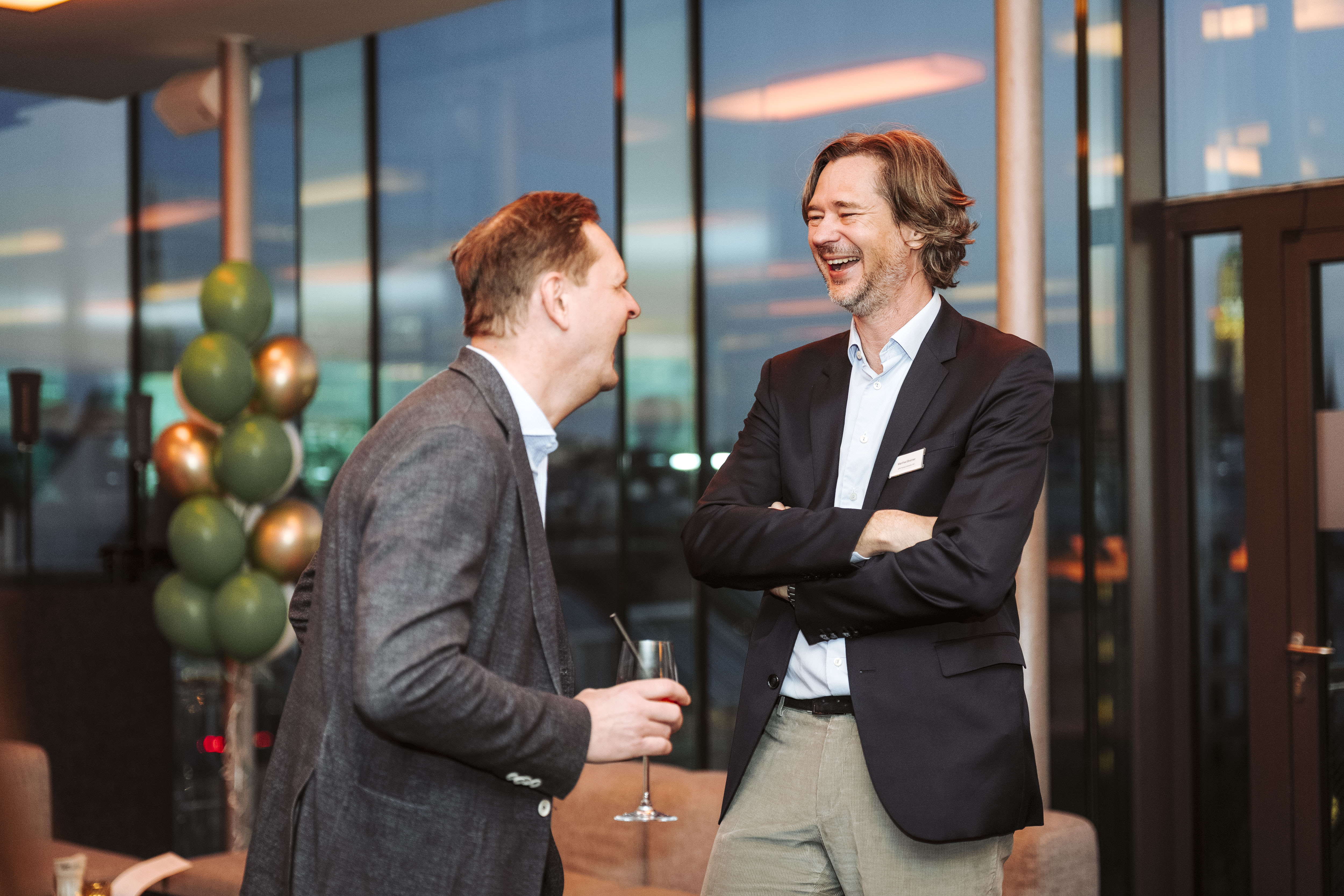 Zwei lachende Geschäftsmänner unterhalten sich auf einer Veranstaltung. Foto von Nadine Studeny.