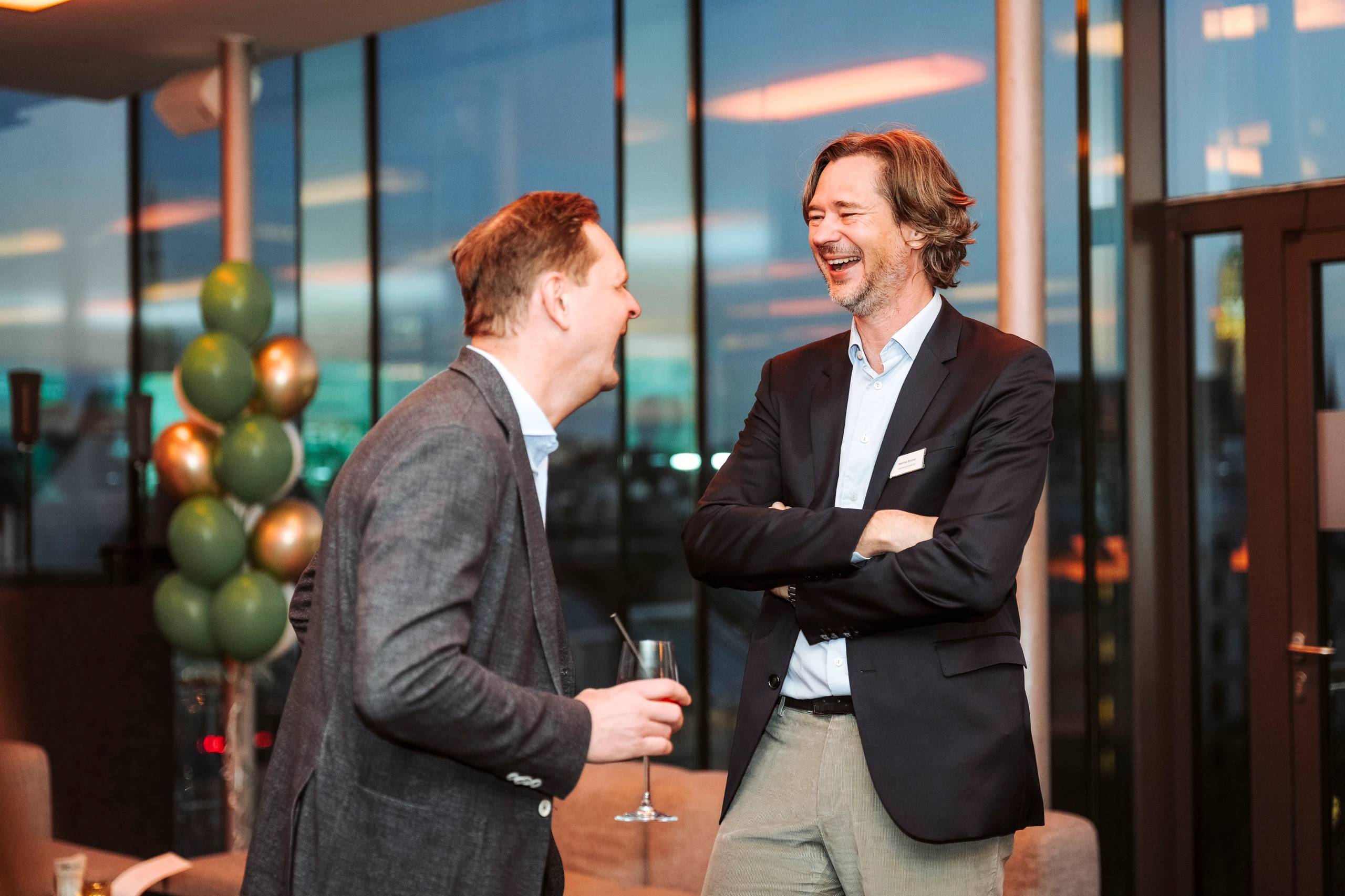 Zwei lachende Geschäftsmänner unterhalten sich auf einer Veranstaltung. Foto von Nadine Studeny.