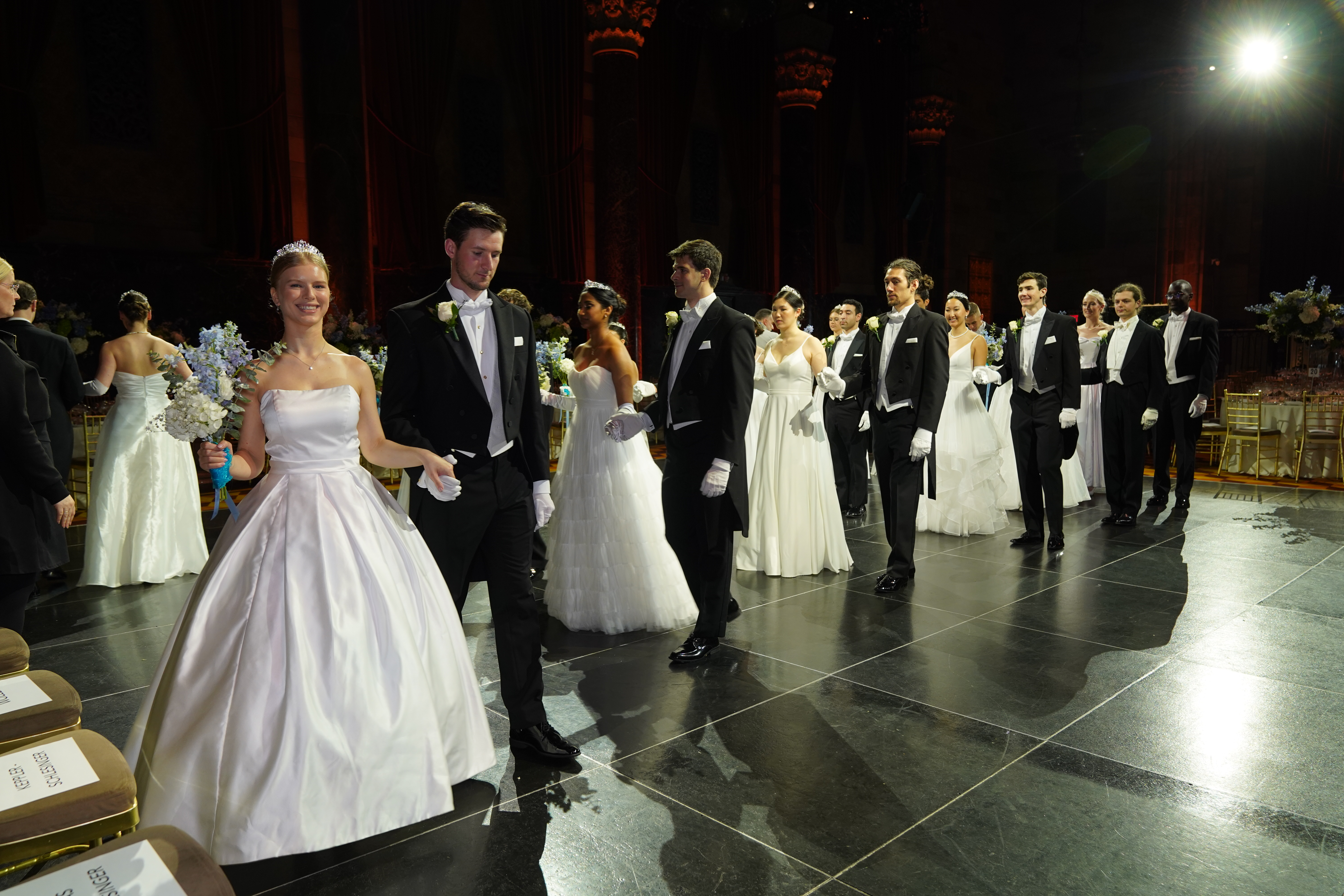 Elegante Paare in weißen Ballkleidern & schwarzen Smokings betreten einen Ballsaal. Festlicher Abend.