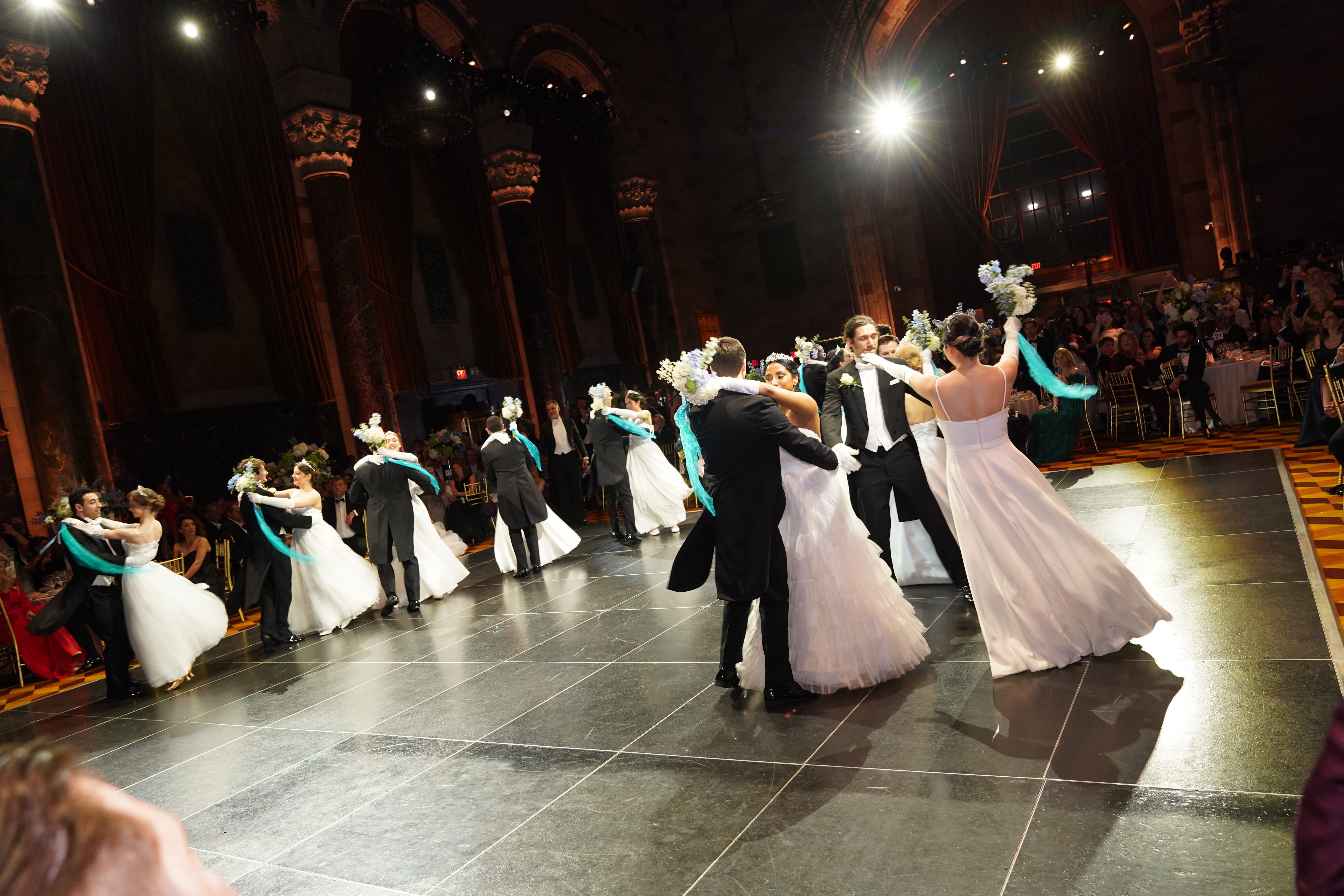 Paare in weißen Ballkleidern und schwarzen Smokings tanzen elegant in einem prächtigen Ballsaal.