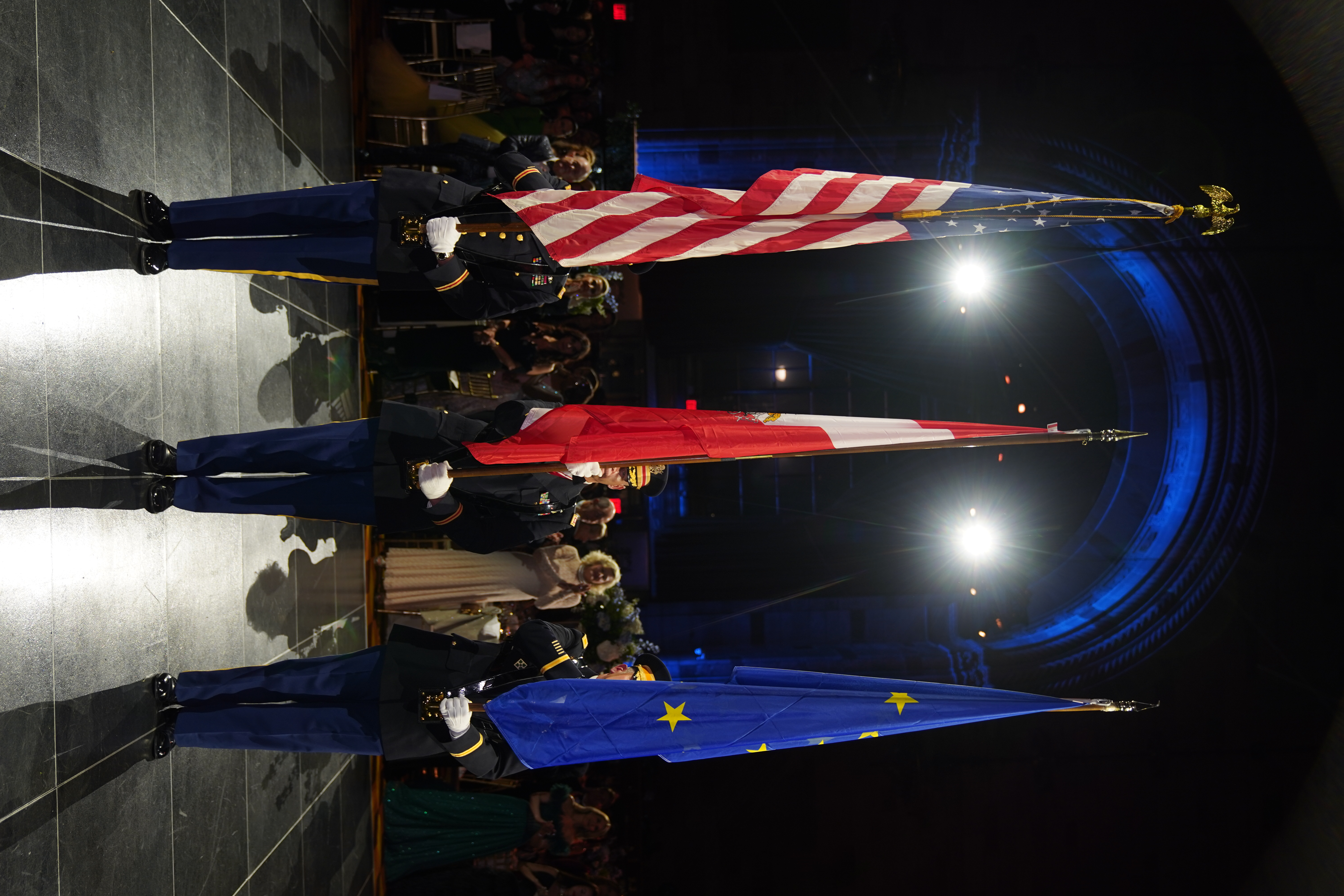 Drei Soldaten in Uniform präsentieren die amerikanische, eine rote und die europäische Flagge bei einer formellen Veranstaltung.