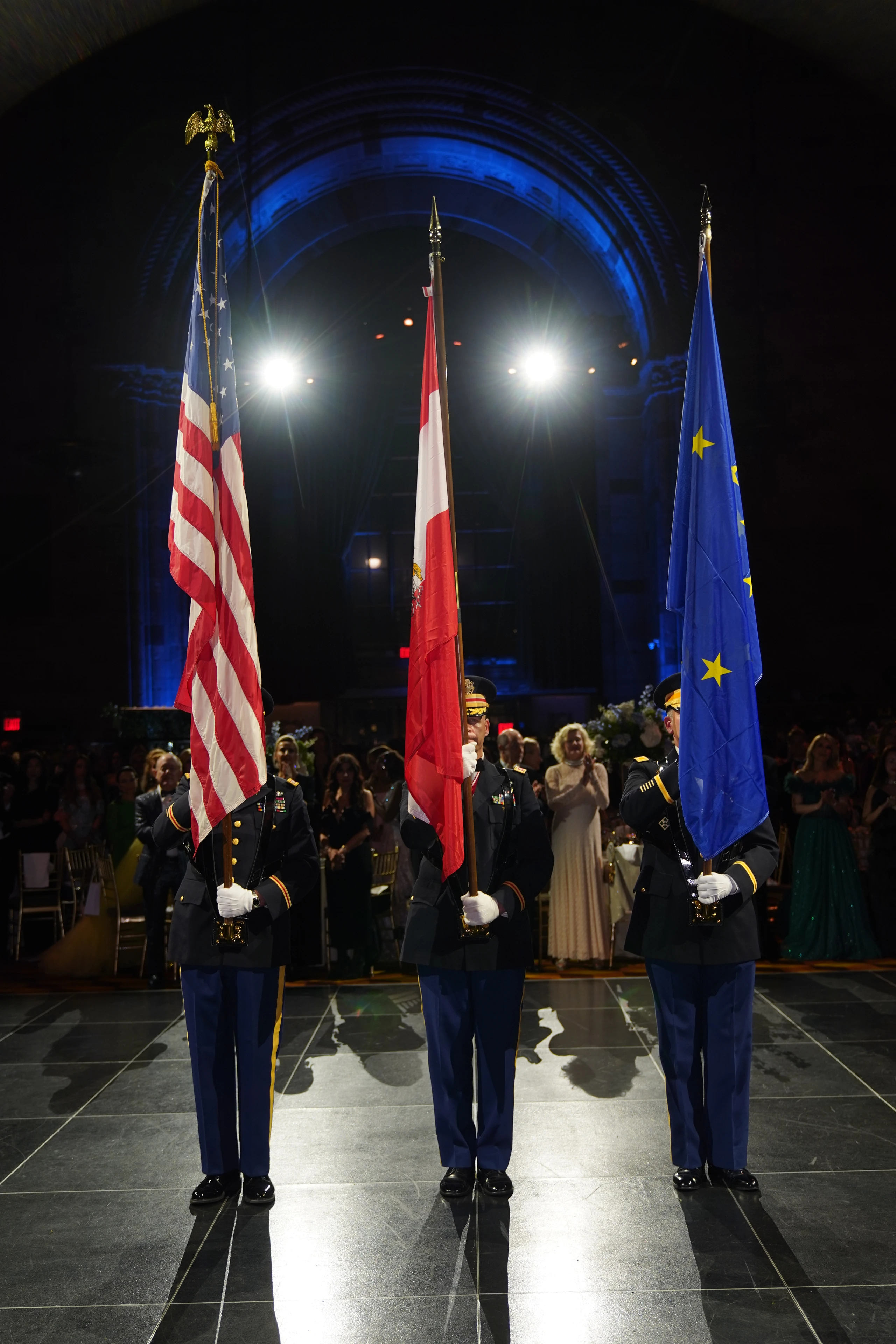 Drei Soldaten in Uniform präsentieren die amerikanische, eine rote und die europäische Flagge bei einer formellen Veranstaltung.