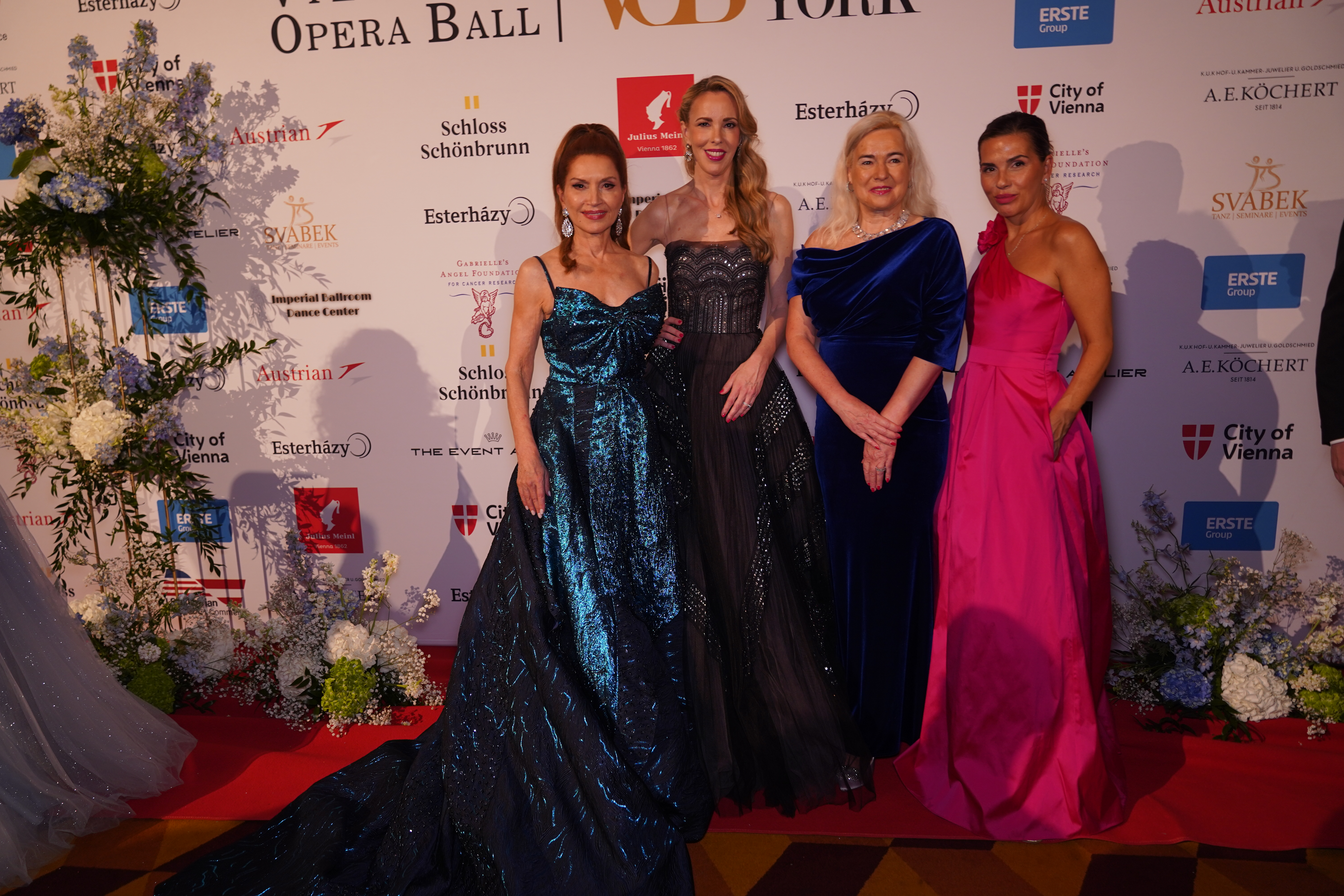 Vier Damen in eleganten Abendkleidern beim Wiener Opernball posieren auf dem roten Teppich.
