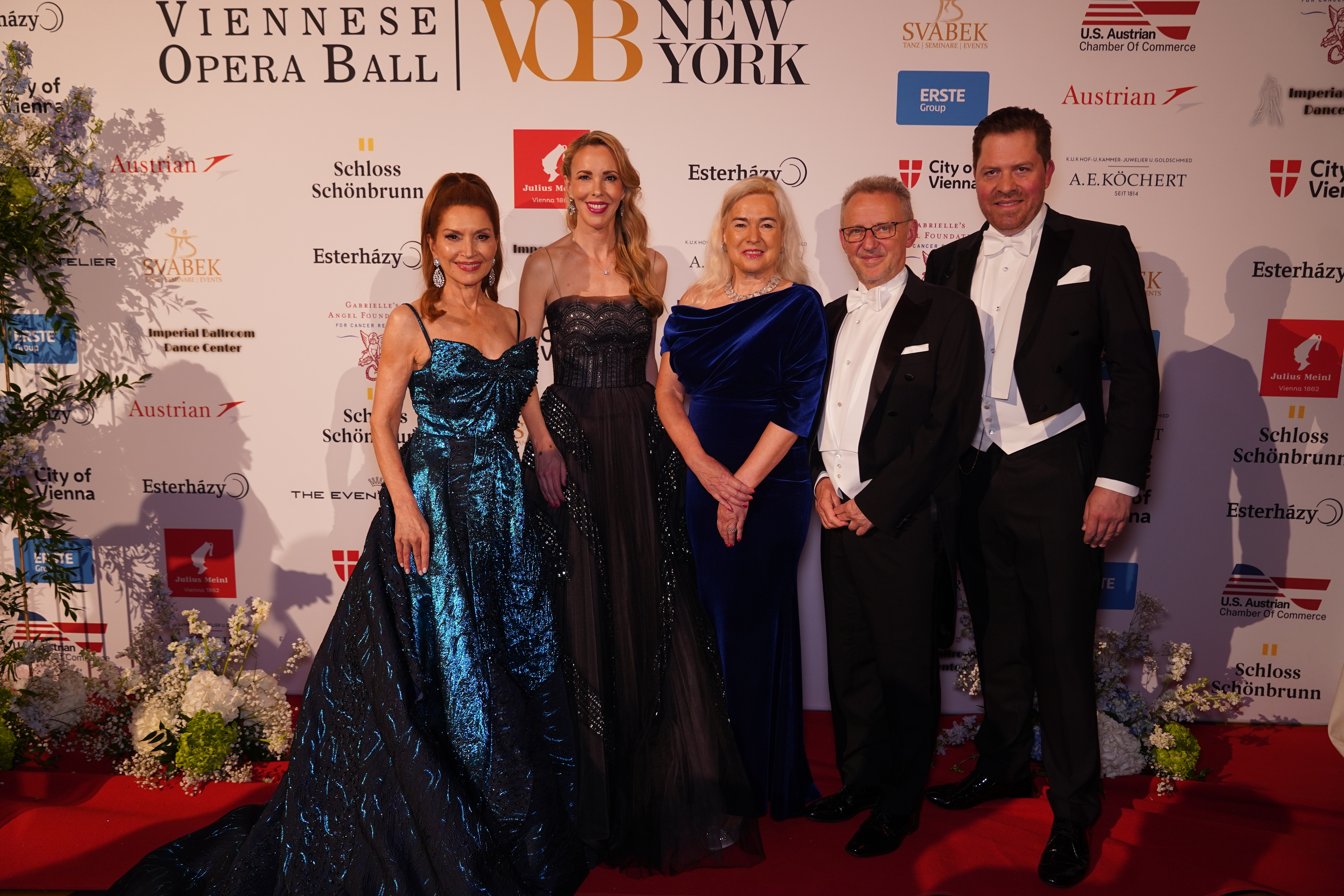 Fünf elegant gekleidete Gäste beim Wiener Opernball New York. Sponsorenlogos im Hintergrund.