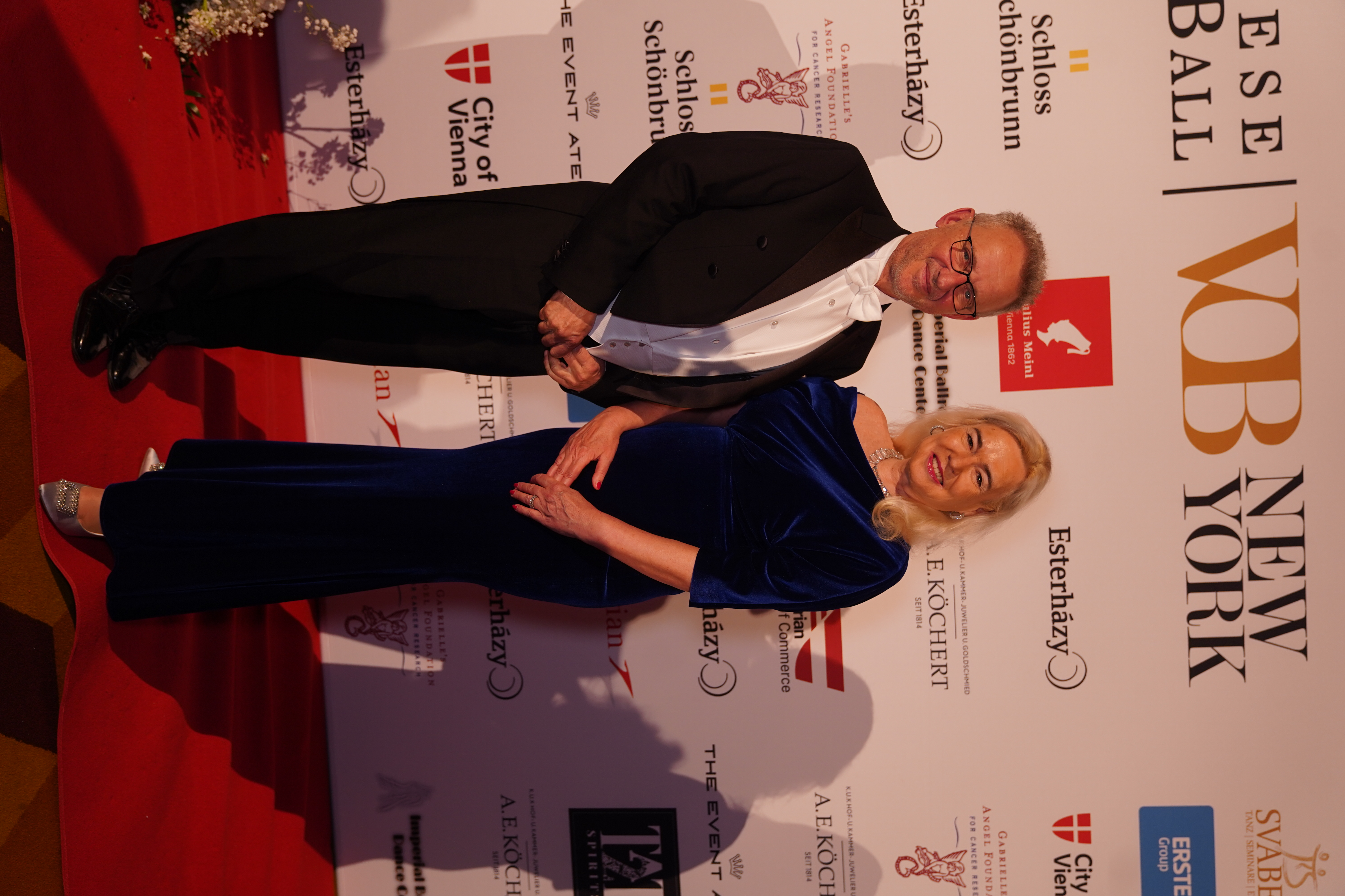 Elegantes Paar beim Esterházy Ball in Wien auf dem roten Teppich. Er trägt Smoking, sie ein dunkelblaues Abendkleid.