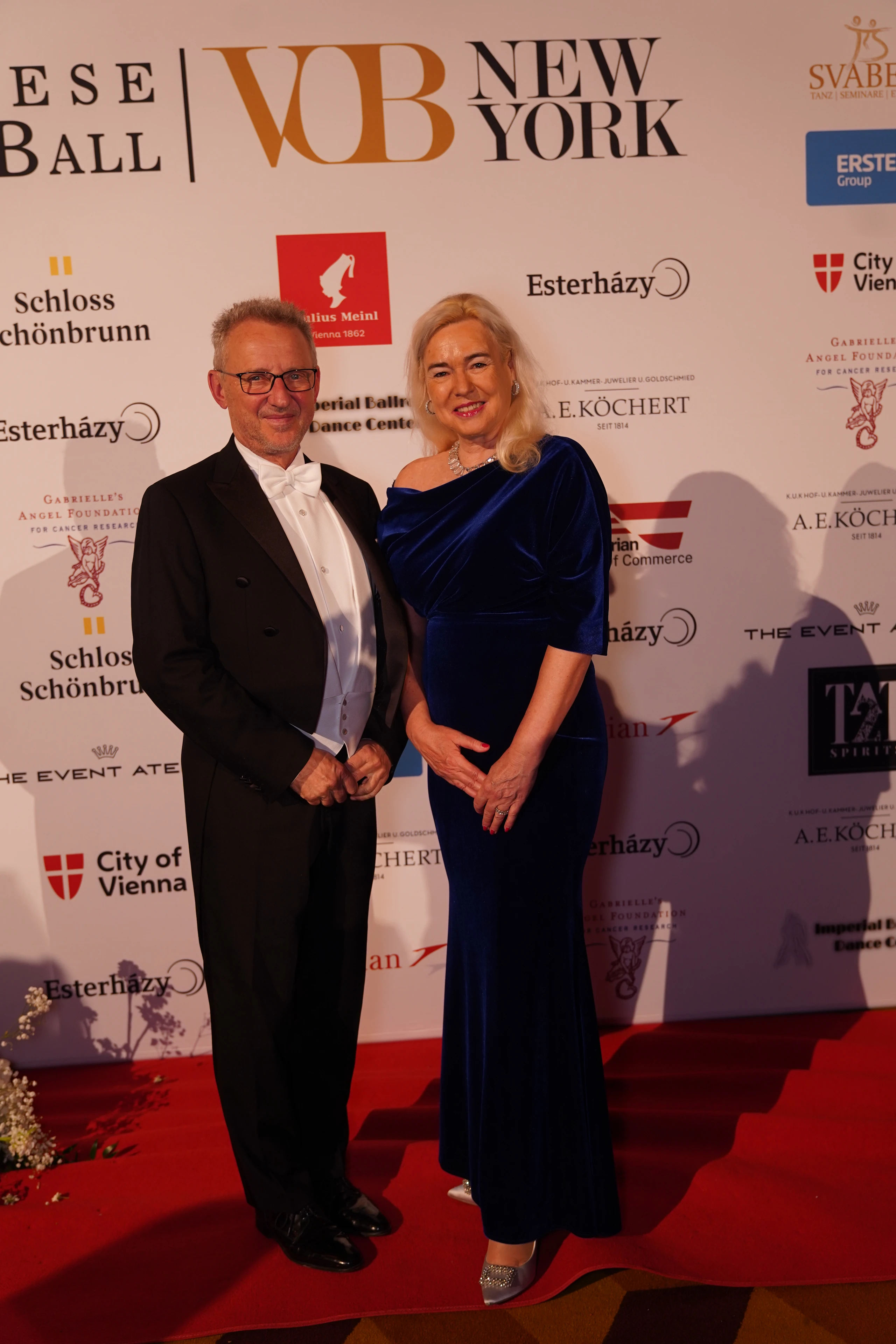 Elegantes Paar beim Esterházy Ball in Wien auf dem roten Teppich. Er trägt Smoking, sie ein dunkelblaues Abendkleid.