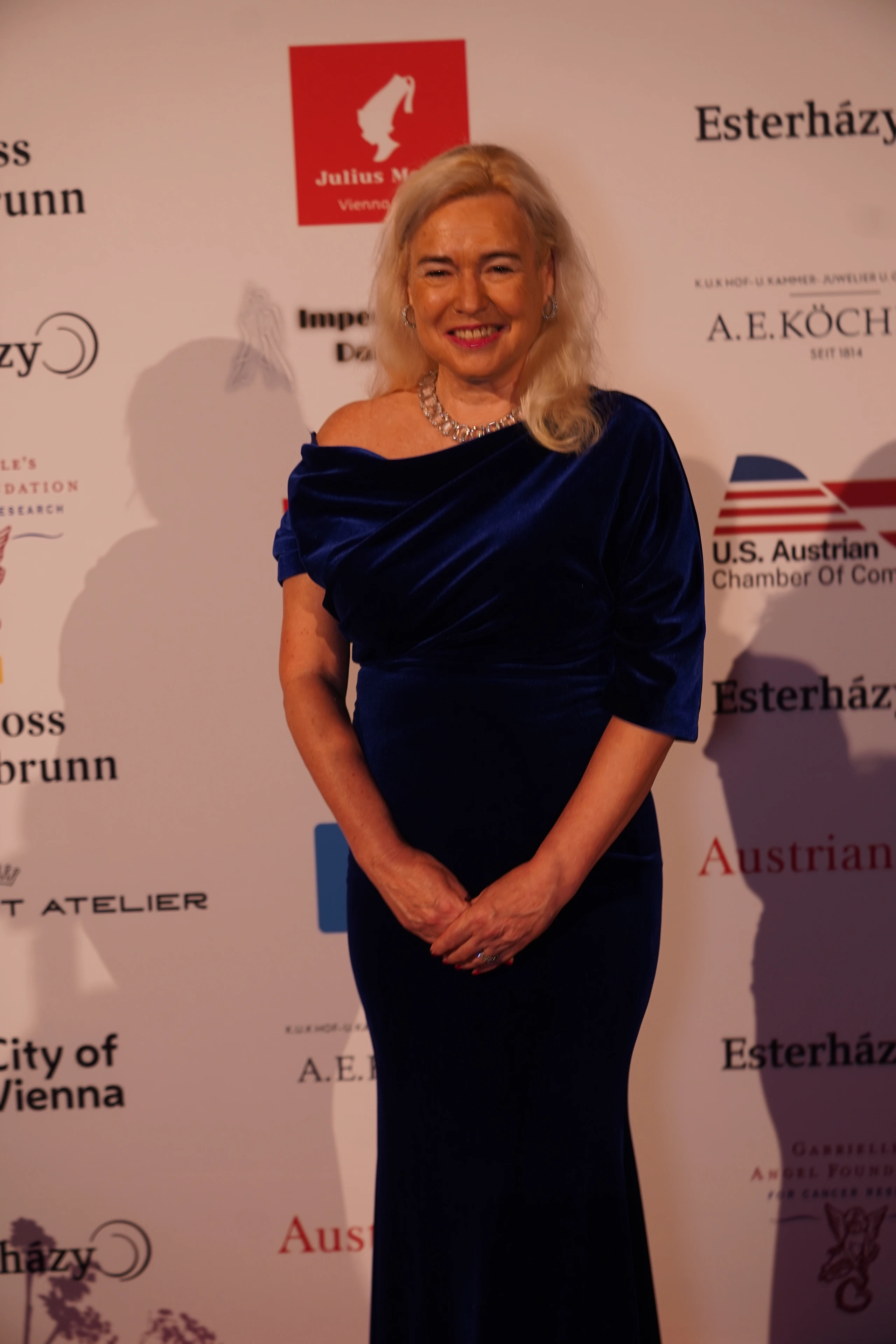Lächelnde Frau in dunkelblauem Samtkleid bei Wiener Veranstaltung. Esterházy, Austrian, City of Vienna Logos sichtbar.