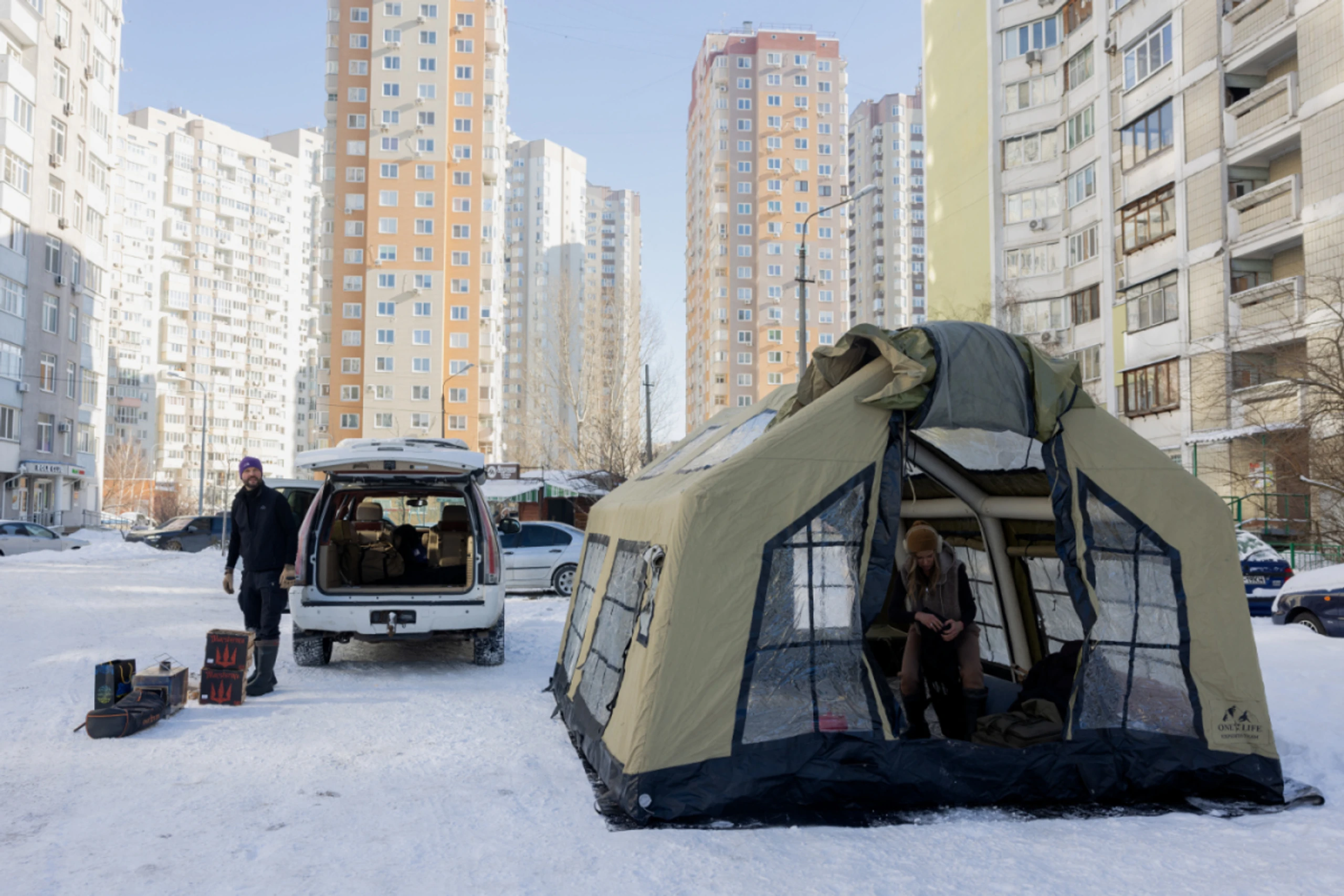 Zelte zum Aufwärmen vor beschädigten, unbeheizten Wohnsilos in Kiew