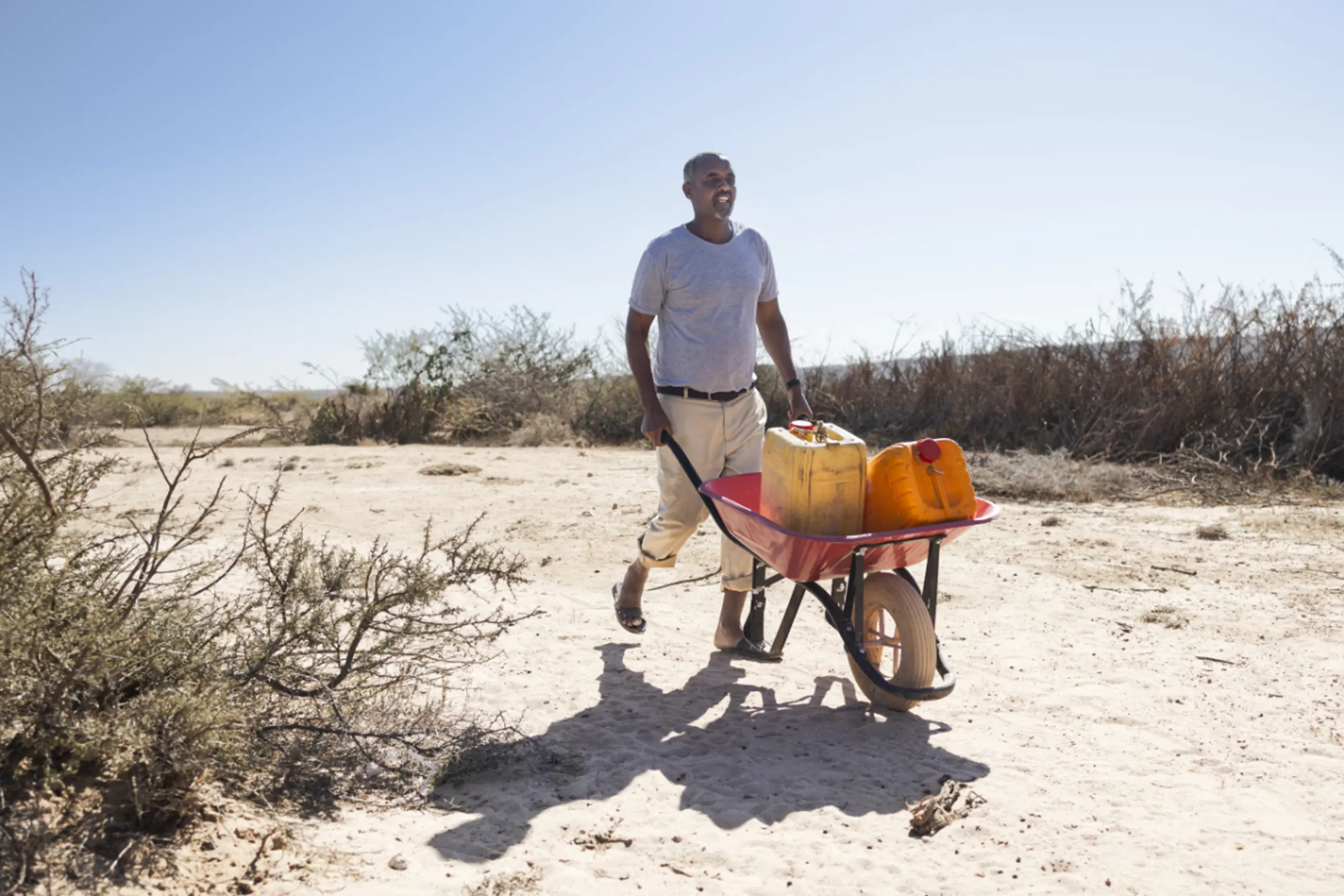 Farmer transportiert in Dürregebiet Wasserkanister mit Scheibtruhe