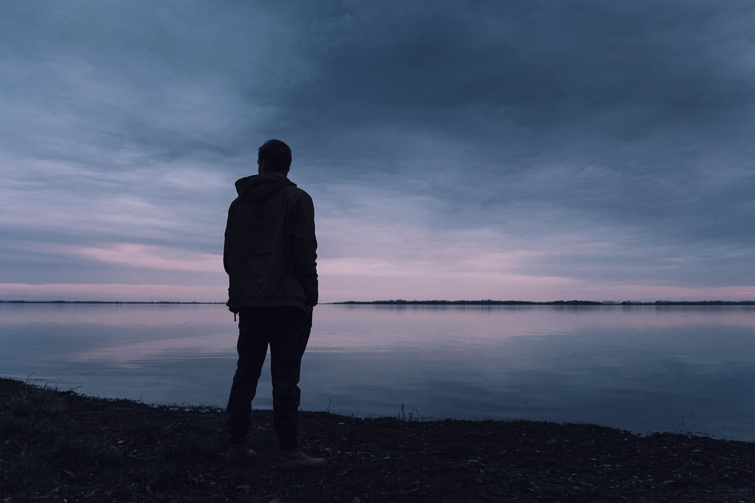 Mann sitzt allein am Meer im Abendlicht