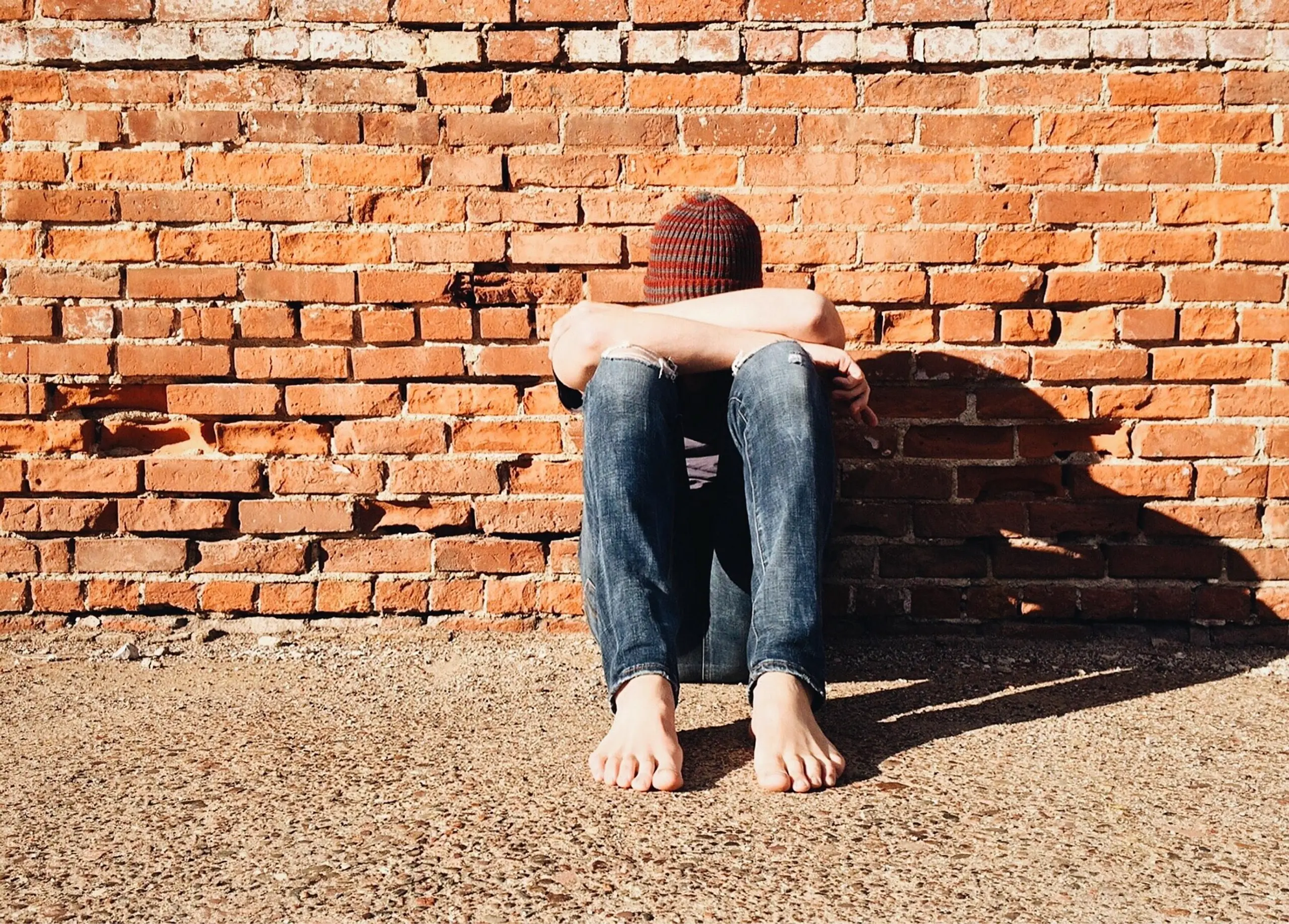 Jugendlicher sitzt allein vor einer Ziegelmauer