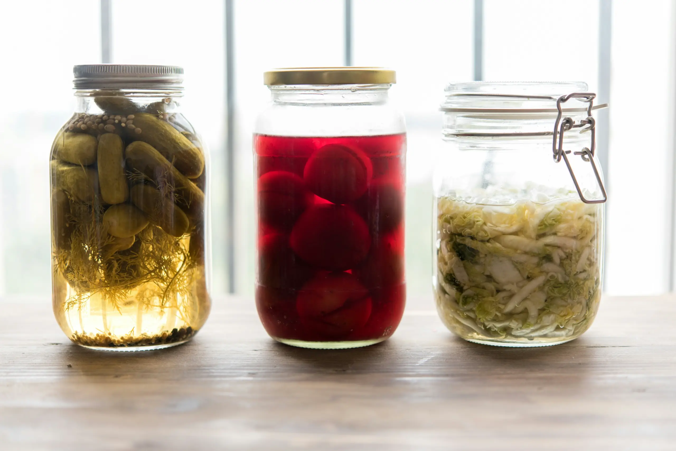 Drei Gläser mit fermentiertem Gemüse, darunter Essiggurken und Sauerkraut