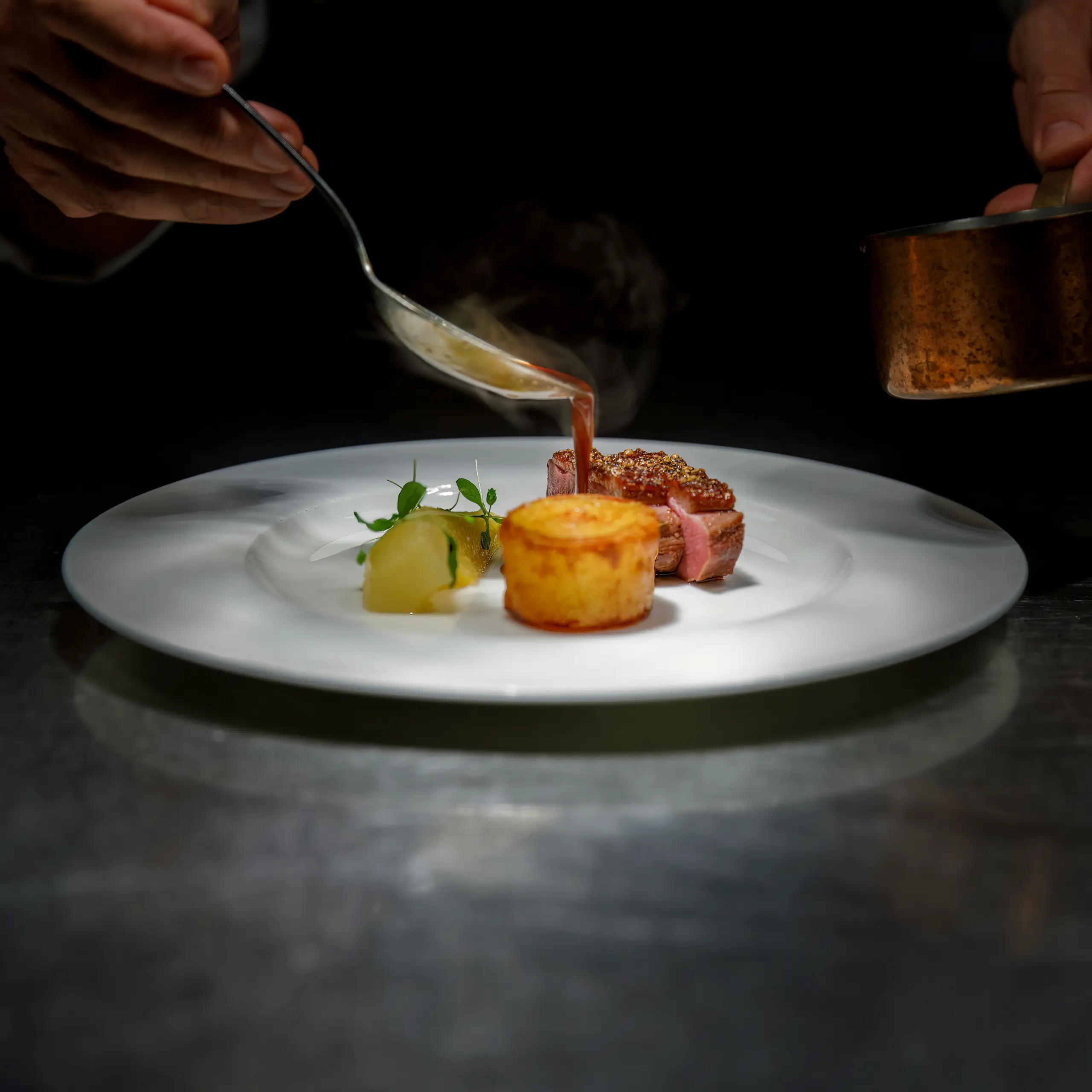 Ein Koch gießt in einer Restaurantküche Sauce über ein angerichtetes Gericht