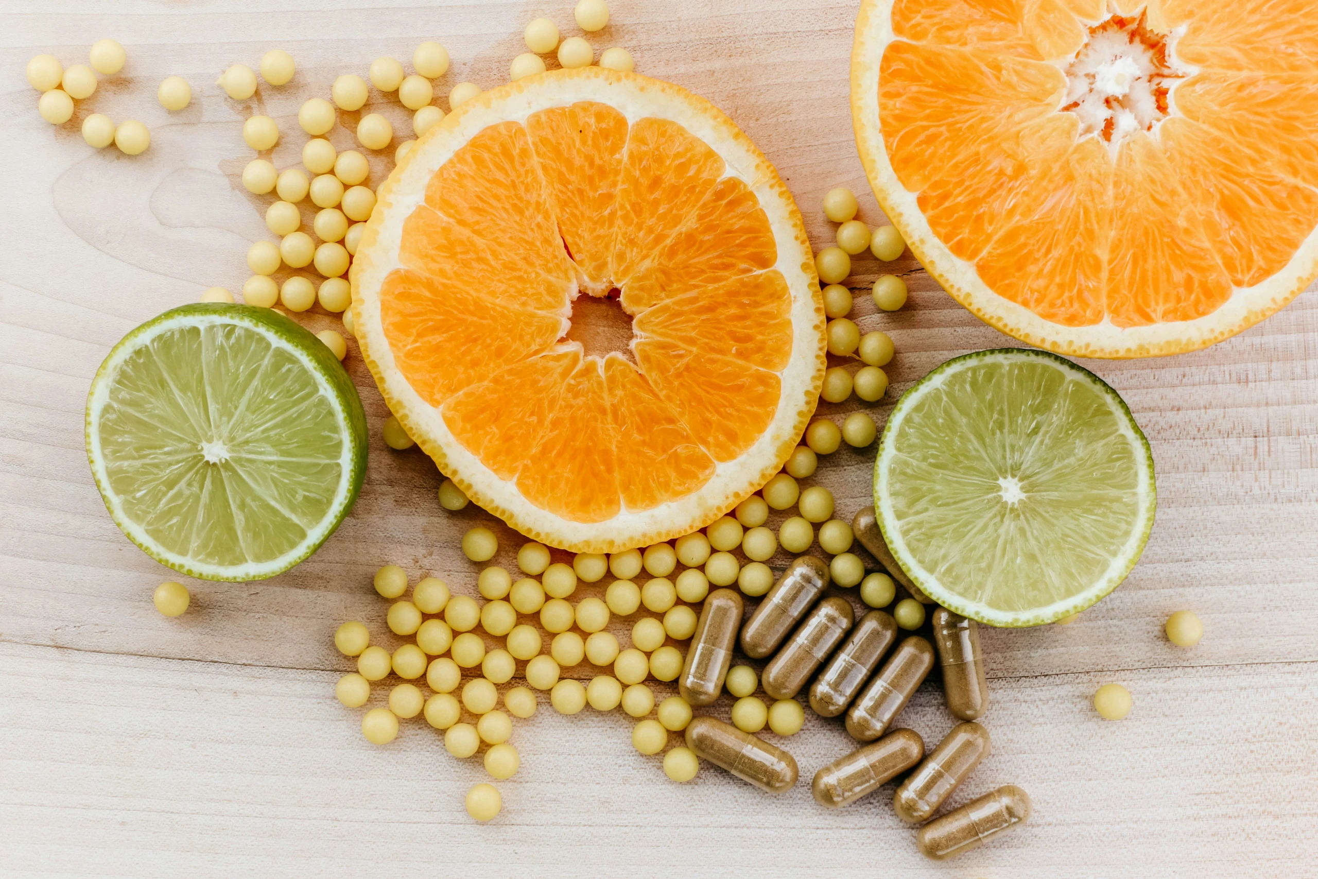 Zitrusscheiben neben Kapseln und Kügelchen eines Nahrungsergänzungsmittels auf einem Holztisch