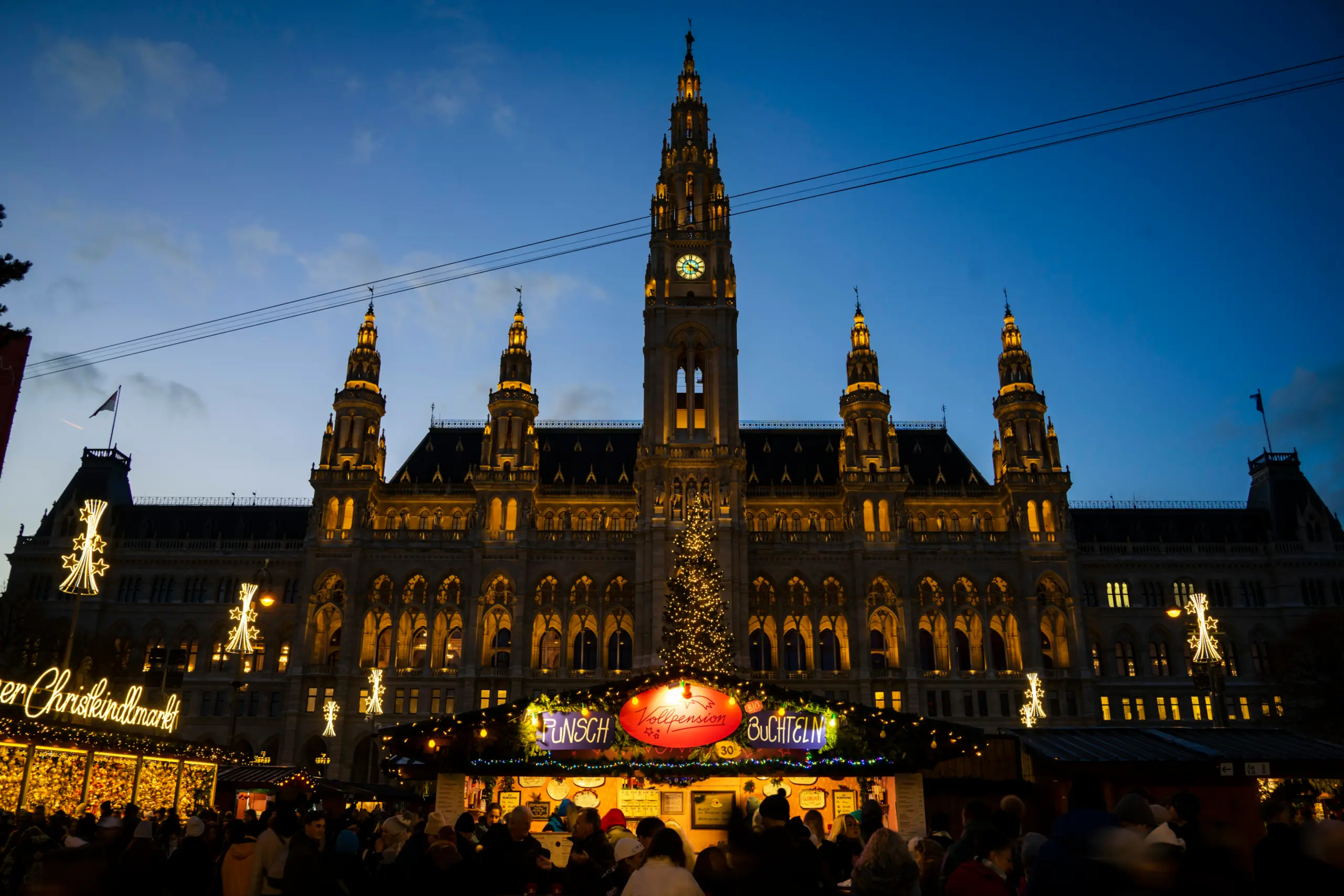 Beleuchteter Weihnachtsmarkt vor einem neugotischen Gebäude in Wien am Abend